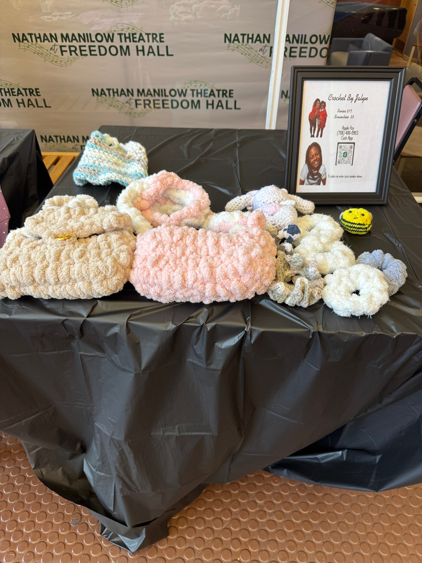 Jalyn's market booth with a table of crochet bags, plushies, and scrunchies